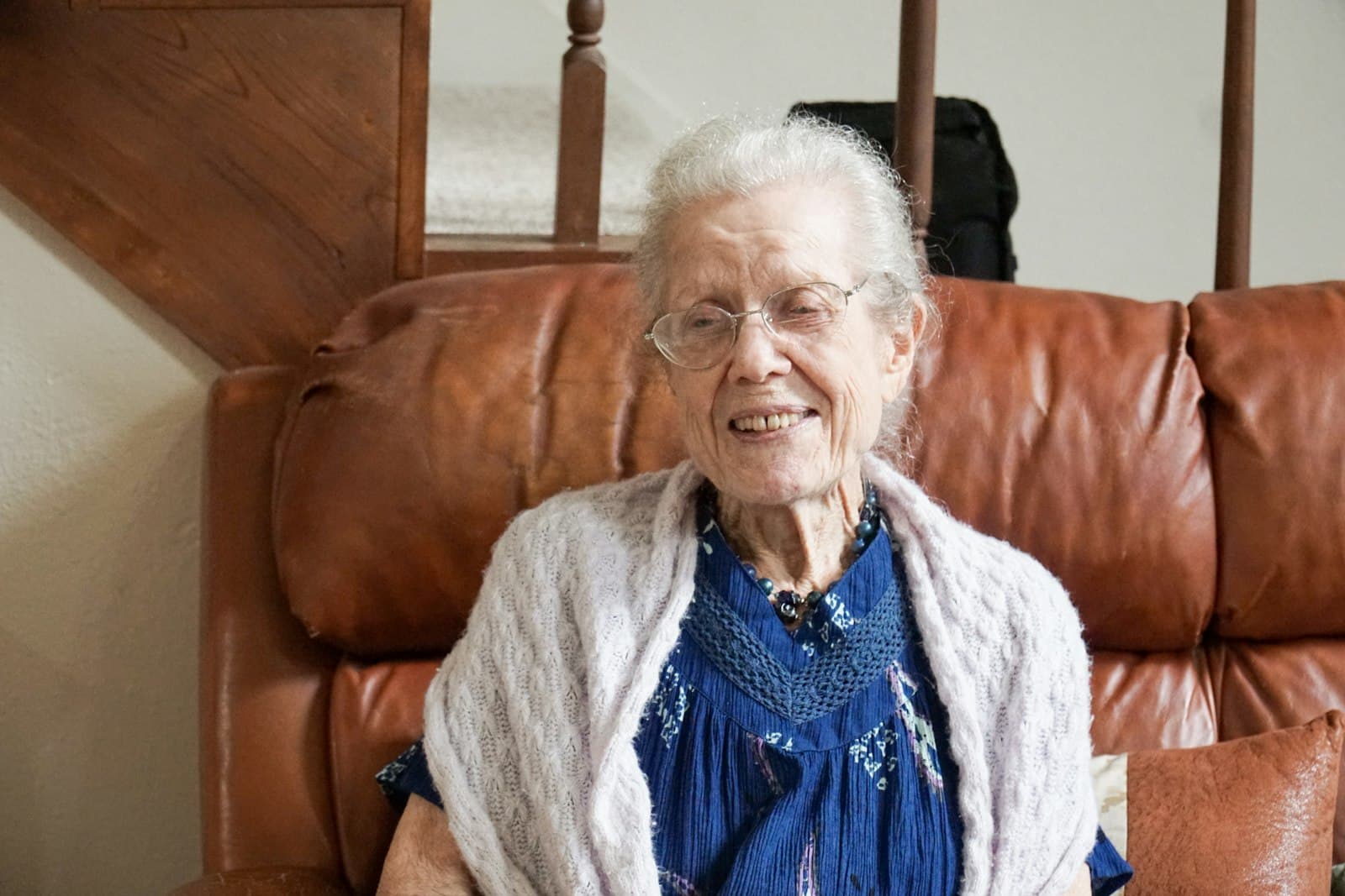 Mujer mayor sonriendo, sentada en el sillón de su casa